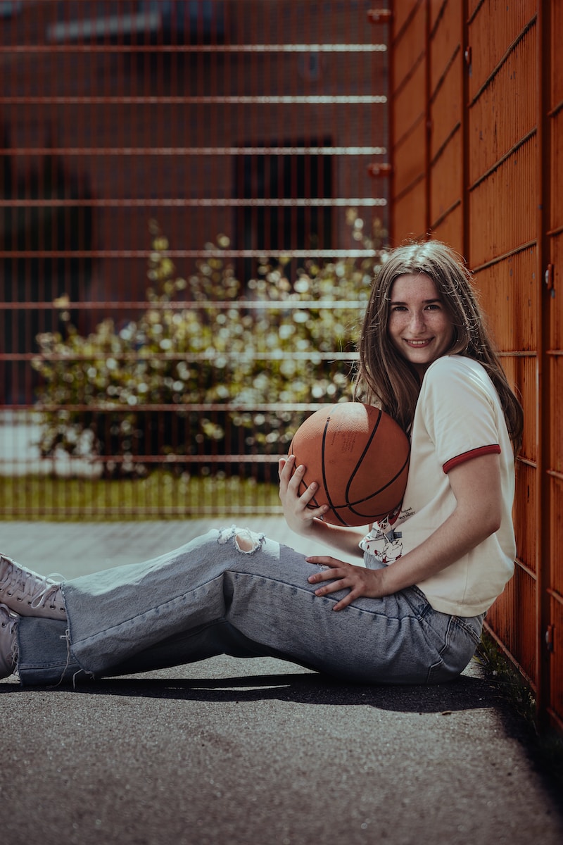 woman in white t-shirt and blue denim jeans sitting on basketball court